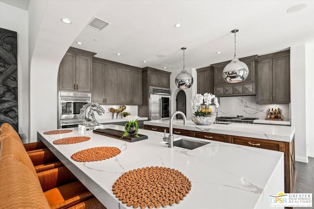 kitchen featuring a spacious island, pendant lighting, appliances with stainless steel finishes, sink, and light stone counters