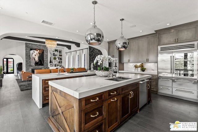 kitchen with decorative light fixtures, dishwasher, a center island with sink, sink, and dark brown cabinetry