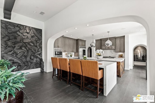 kitchen featuring an island with sink, dark hardwood / wood-style floors, decorative light fixtures, built in fridge, and dark brown cabinetry