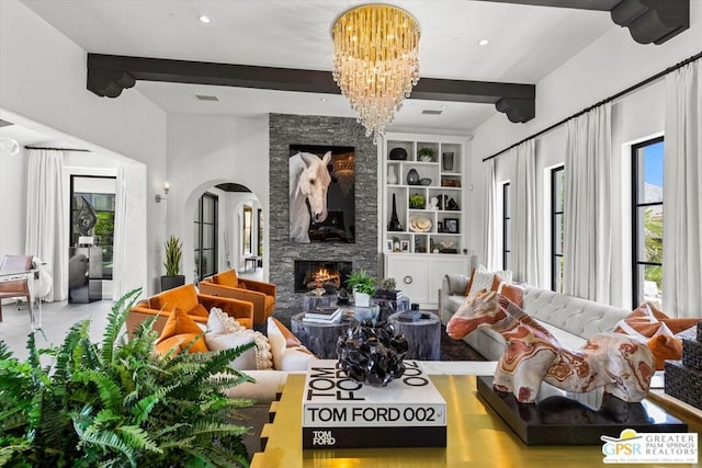 living room with built in features, beamed ceiling, a stone fireplace, and a chandelier