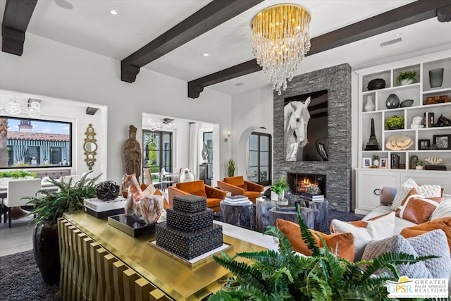 living room featuring built in shelves, beam ceiling, a stone fireplace, and an inviting chandelier