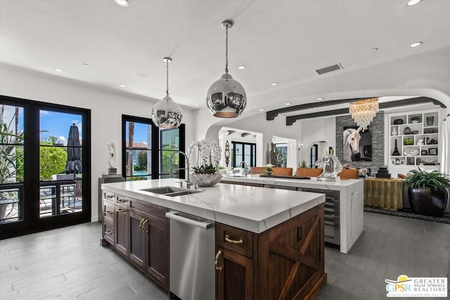 kitchen featuring pendant lighting, beam ceiling, a center island with sink, sink, and dark brown cabinets