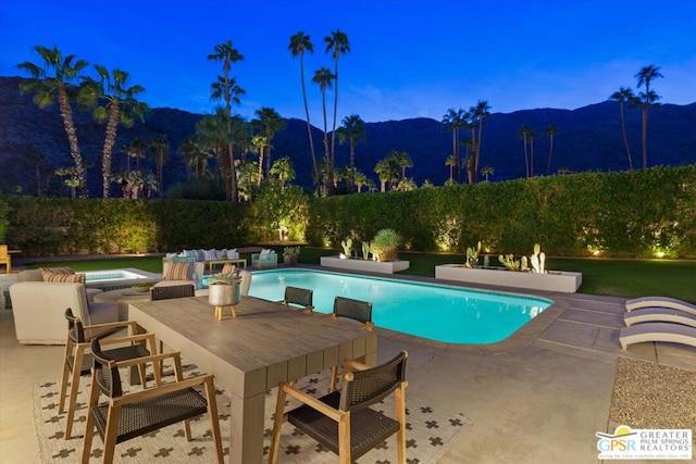 pool at dusk featuring a patio area, a mountain view, and an in ground hot tub