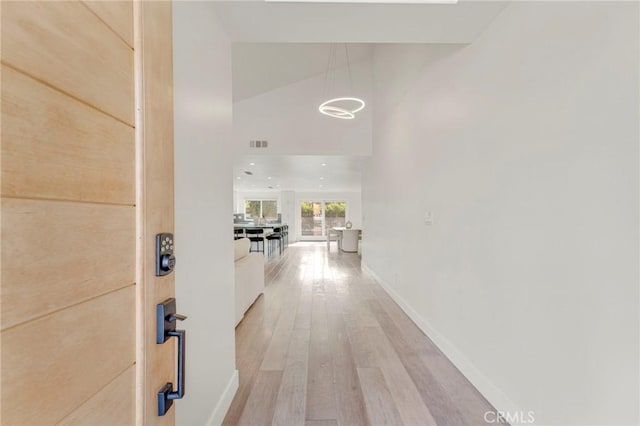 hall featuring light wood-type flooring and a towering ceiling