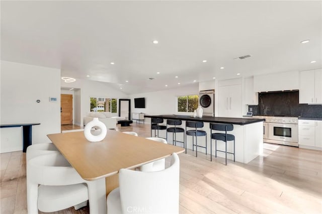 dining area featuring stacked washer and dryer, lofted ceiling, and light wood-type flooring