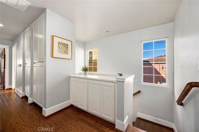 corridor featuring dark wood-type flooring, an upstairs landing, and baseboards