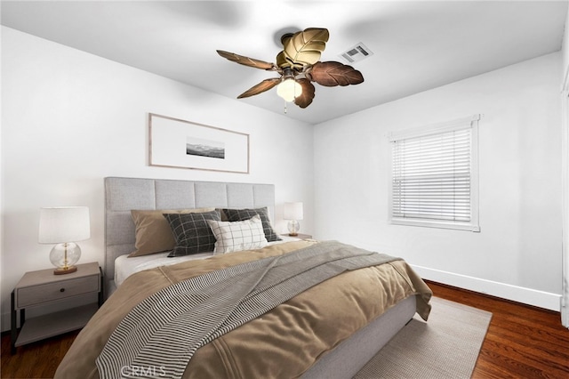 bedroom with a ceiling fan, visible vents, baseboards, and wood finished floors