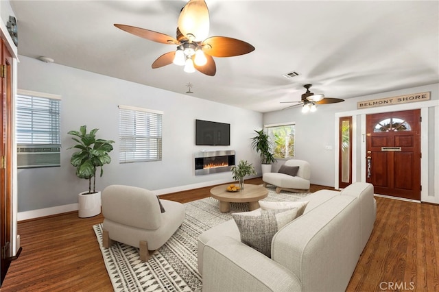 living area with a glass covered fireplace, wood finished floors, visible vents, and a healthy amount of sunlight