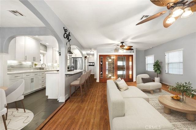 living area with ceiling fan, dark wood-type flooring, visible vents, and baseboards