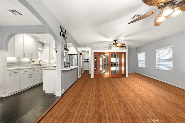 unfurnished living room featuring ceiling fan, a sink, visible vents, baseboards, and dark wood finished floors