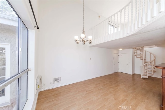 unfurnished living room featuring hardwood / wood-style flooring, a high ceiling, and a chandelier