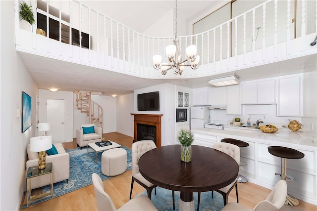 dining area featuring an inviting chandelier, sink, a high ceiling, and light hardwood / wood-style floors