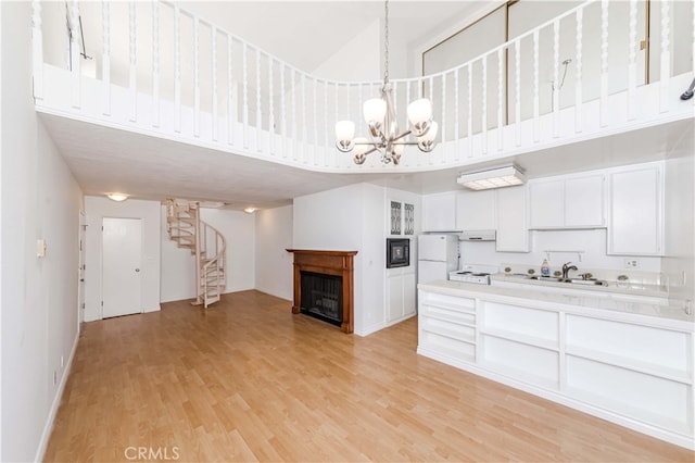 kitchen with a high ceiling, light wood-type flooring, a chandelier, white cabinetry, and white appliances