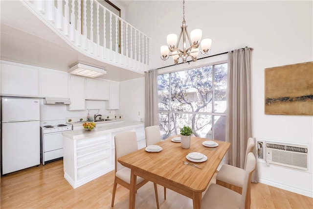 dining space with light hardwood / wood-style floors, a chandelier, sink, and a towering ceiling