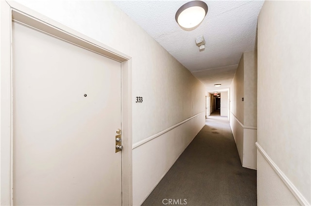 hall featuring dark colored carpet and a textured ceiling