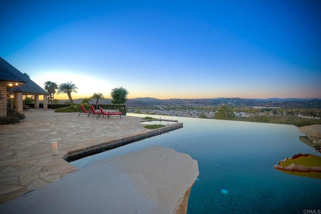 pool at dusk featuring a mountain view and a patio