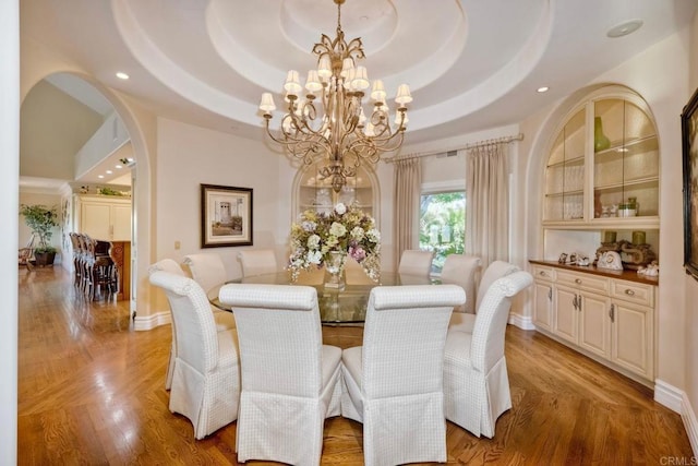 dining space with light wood-type flooring, a tray ceiling, and an inviting chandelier