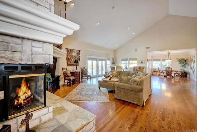 living room with light wood-type flooring, high vaulted ceiling, and a stone fireplace