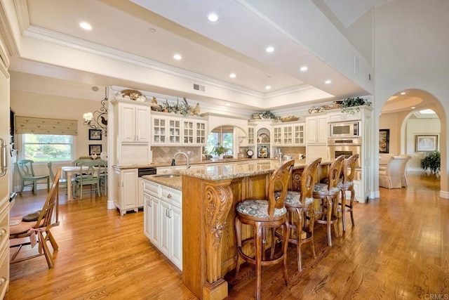 kitchen with light stone countertops, light hardwood / wood-style floors, a spacious island, decorative backsplash, and appliances with stainless steel finishes