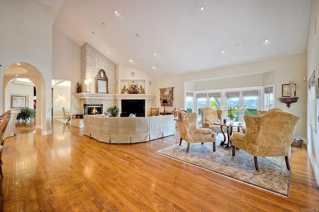 living room featuring a large fireplace, high vaulted ceiling, and light wood-type flooring