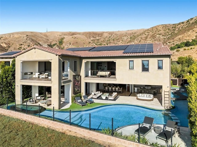 rear view of house featuring solar panels, a mountain view, a balcony, and an outdoor hangout area