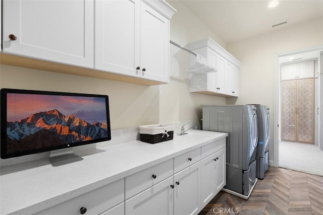 clothes washing area with visible vents, a sink, washing machine and clothes dryer, and cabinet space