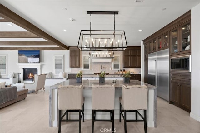 kitchen featuring a warm lit fireplace, a breakfast bar area, glass insert cabinets, built in appliances, and a large island with sink