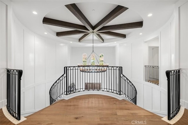 stairs with coffered ceiling, a decorative wall, a notable chandelier, and beamed ceiling