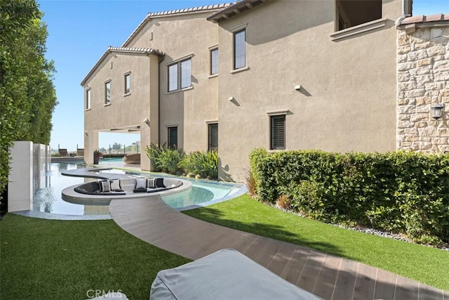 back of house featuring an outdoor pool, a tile roof, a lawn, and stucco siding