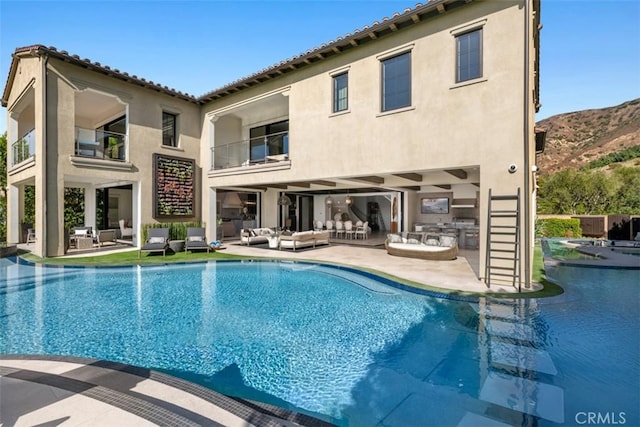 back of property featuring stucco siding, a balcony, exterior kitchen, an outdoor pool, and an outdoor living space