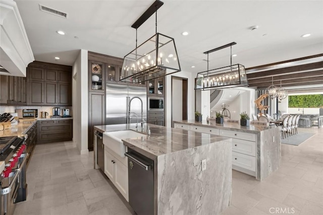 kitchen with glass insert cabinets, white cabinetry, dark brown cabinetry, an island with sink, and built in appliances