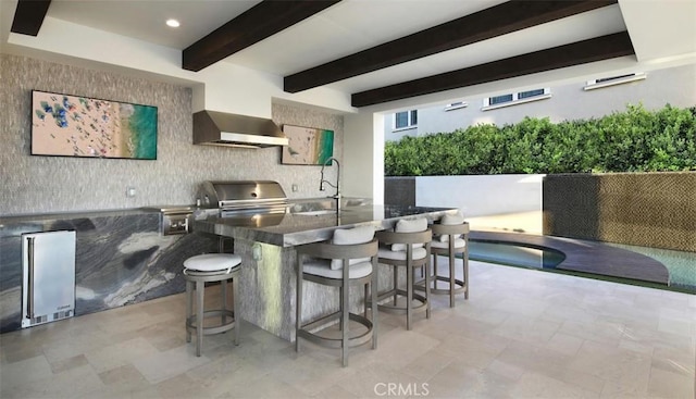 kitchen with dark countertops, wall chimney exhaust hood, high quality fridge, a breakfast bar area, and a sink