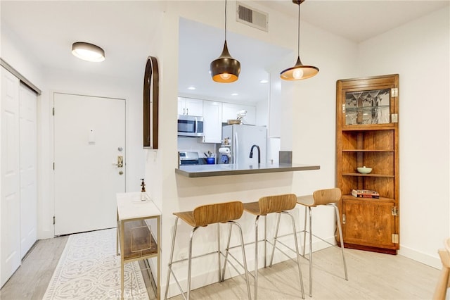 kitchen featuring kitchen peninsula, white cabinets, light wood-type flooring, pendant lighting, and white fridge