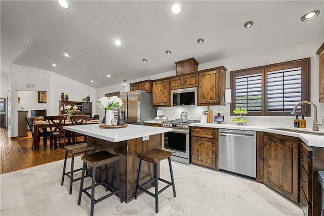 kitchen with sink, a center island, stainless steel appliances, lofted ceiling, and a breakfast bar