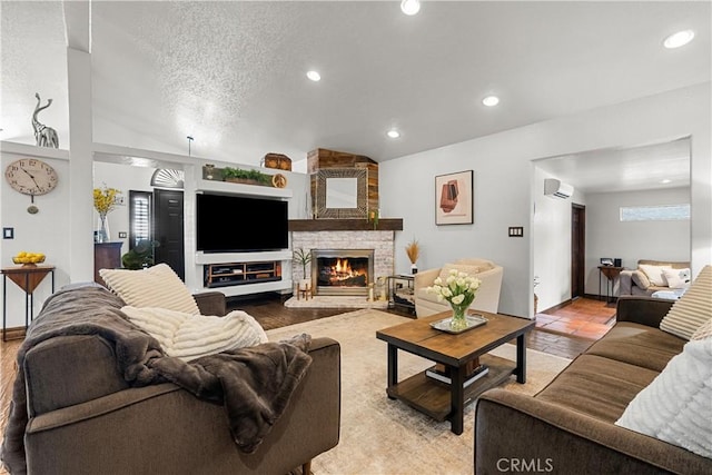 living room with a textured ceiling, an AC wall unit, light hardwood / wood-style flooring, a stone fireplace, and lofted ceiling