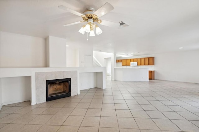 unfurnished living room with light tile patterned flooring, ceiling fan, and a tile fireplace