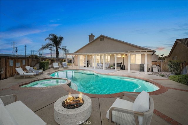 pool at dusk with an in ground hot tub, a patio, and a fire pit