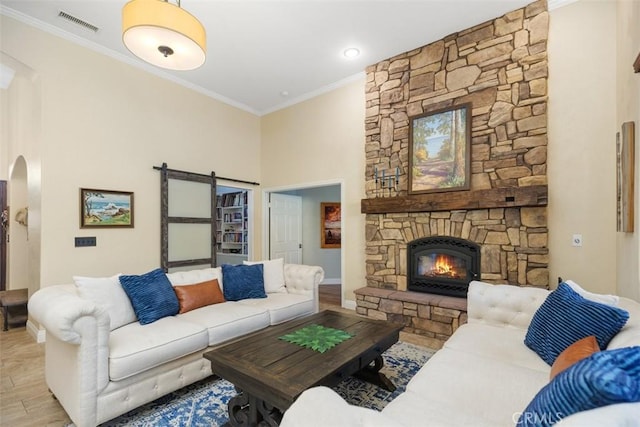 living room featuring a barn door, a stone fireplace, light wood-type flooring, and crown molding