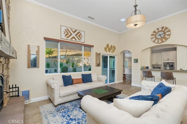 living room with a high ceiling, a stone fireplace, and crown molding