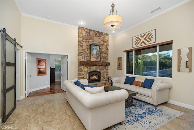 living room with a stone fireplace, a barn door, crown molding, a towering ceiling, and light wood-type flooring