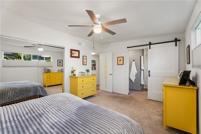 carpeted bedroom with ceiling fan, a closet, and a barn door