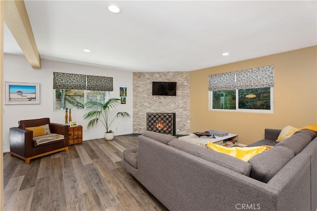 living room featuring beam ceiling, hardwood / wood-style flooring, and a stone fireplace