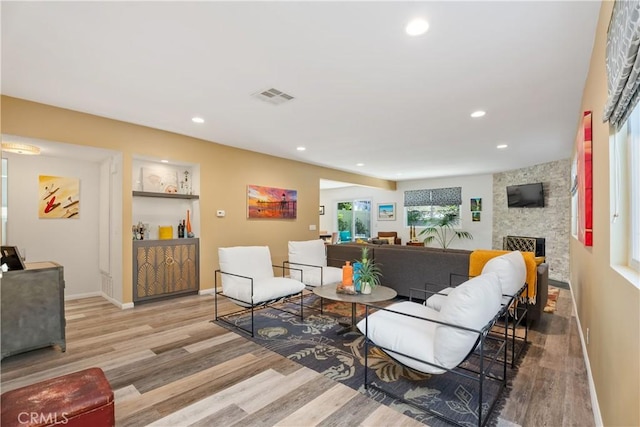 living room with light wood-type flooring, a stone fireplace, and built in shelves