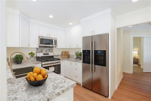 kitchen featuring stainless steel appliances, light stone countertops, light hardwood / wood-style floors, and white cabinetry