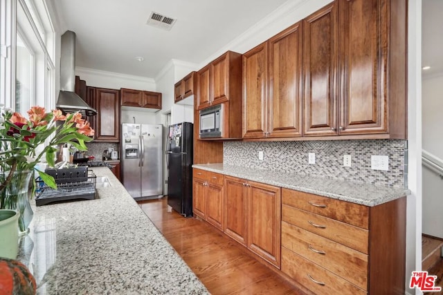 kitchen with wall chimney exhaust hood, tasteful backsplash, appliances with stainless steel finishes, and light hardwood / wood-style flooring