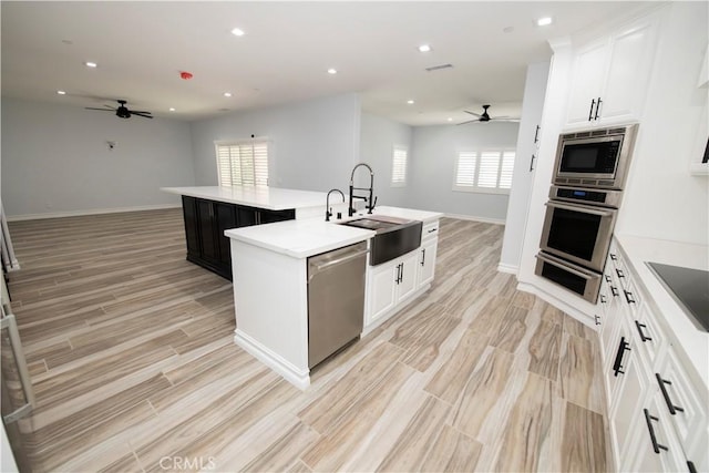 kitchen featuring light wood-type flooring, stainless steel appliances, a kitchen island with sink, sink, and white cabinetry