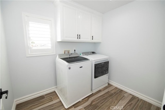 clothes washing area featuring separate washer and dryer, cabinets, and wood-type flooring