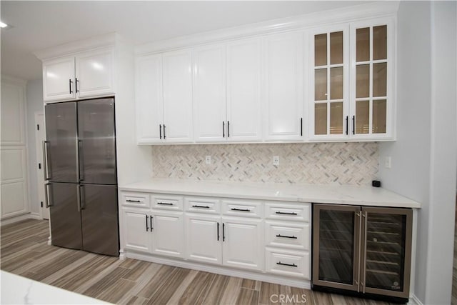 kitchen featuring light wood-type flooring, backsplash, beverage cooler, white cabinetry, and stainless steel refrigerator