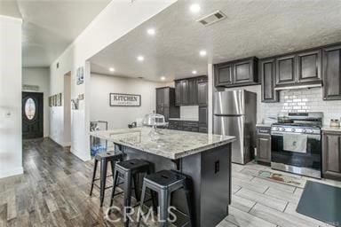 kitchen featuring light stone countertops, a breakfast bar area, a center island with sink, appliances with stainless steel finishes, and light wood-type flooring