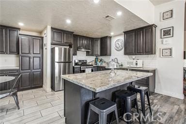 kitchen featuring light hardwood / wood-style flooring, appliances with stainless steel finishes, a kitchen island, a kitchen bar, and dark brown cabinetry